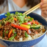 How Much Protein in Ground Beef: Everything You Need to Know 15 A vibrant bowl of high-protein ground beef stir-fry served over rice, garnished with sesame seeds, fresh cilantro, and green onions.
